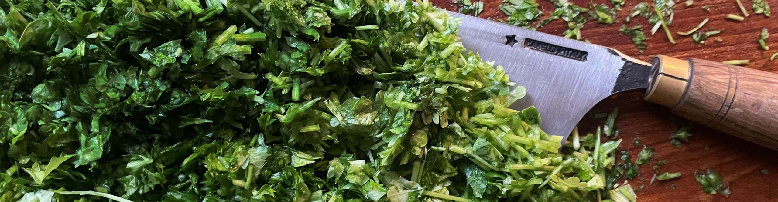 Chopped Parsley on a wooden cutting board with a traditional, exclusive Italian knife to symbolize the love for the process of audio editing in Hindenburg Pro, reflecting the precision, skill, and dedication required to craft a high-quality and refined result.